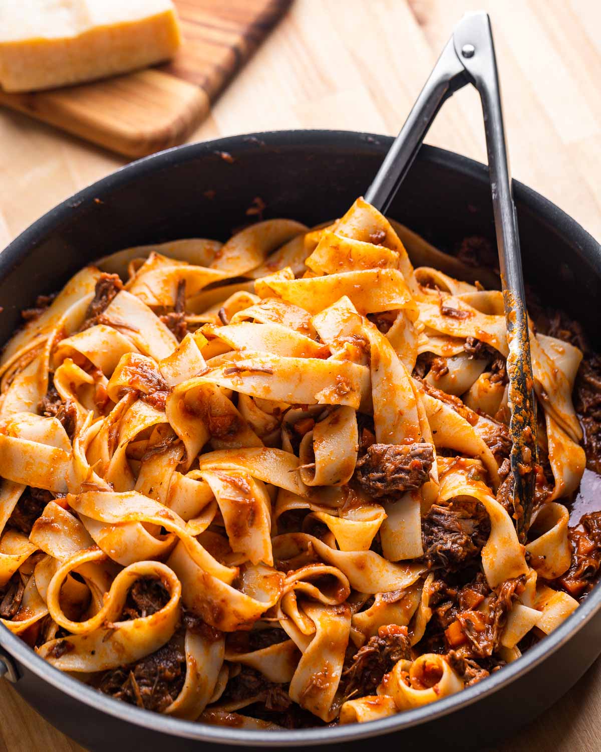 Large pan with short rib pappardelle on wood table.