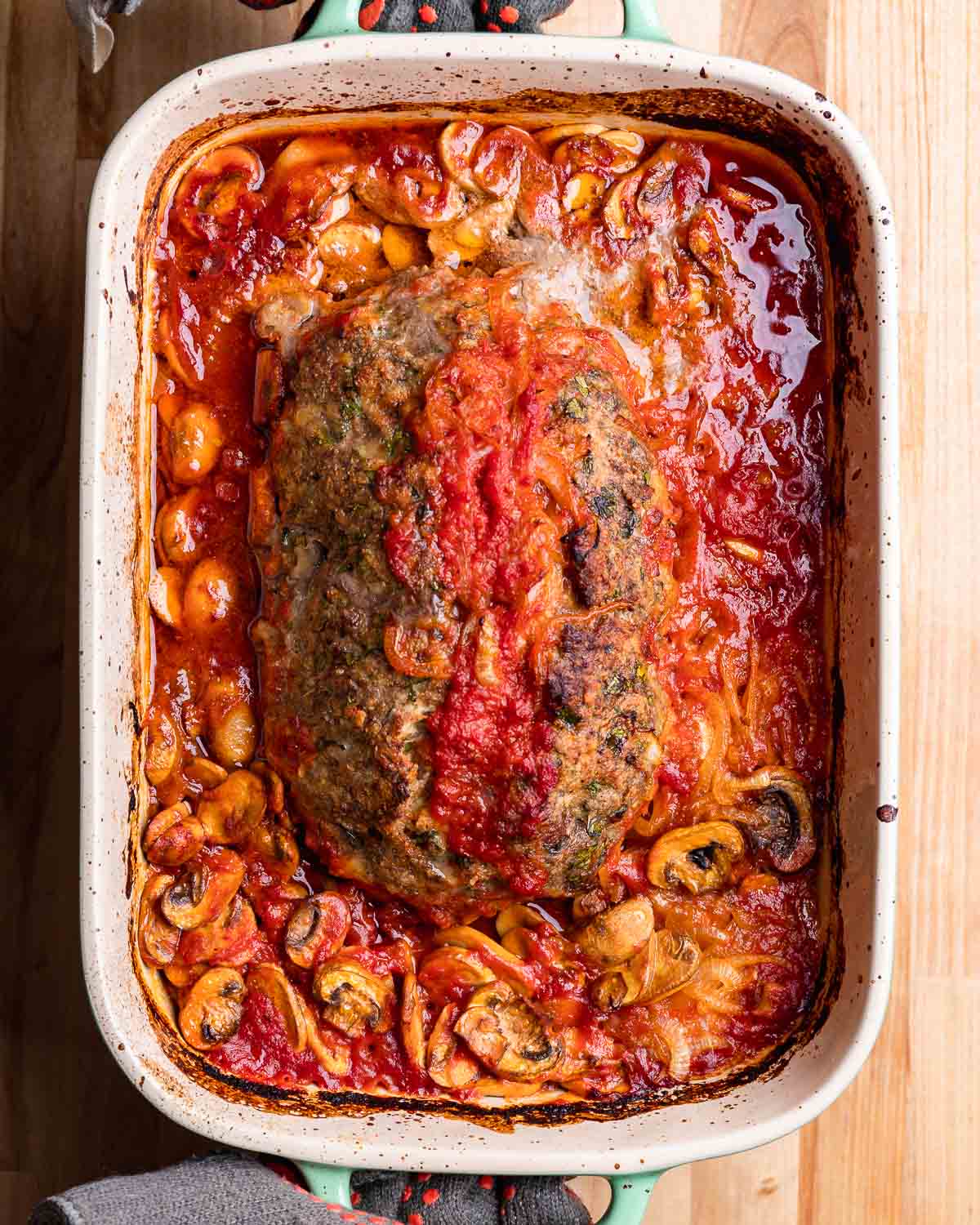 Gloved hands holding baking dish with cooked meatloaf.