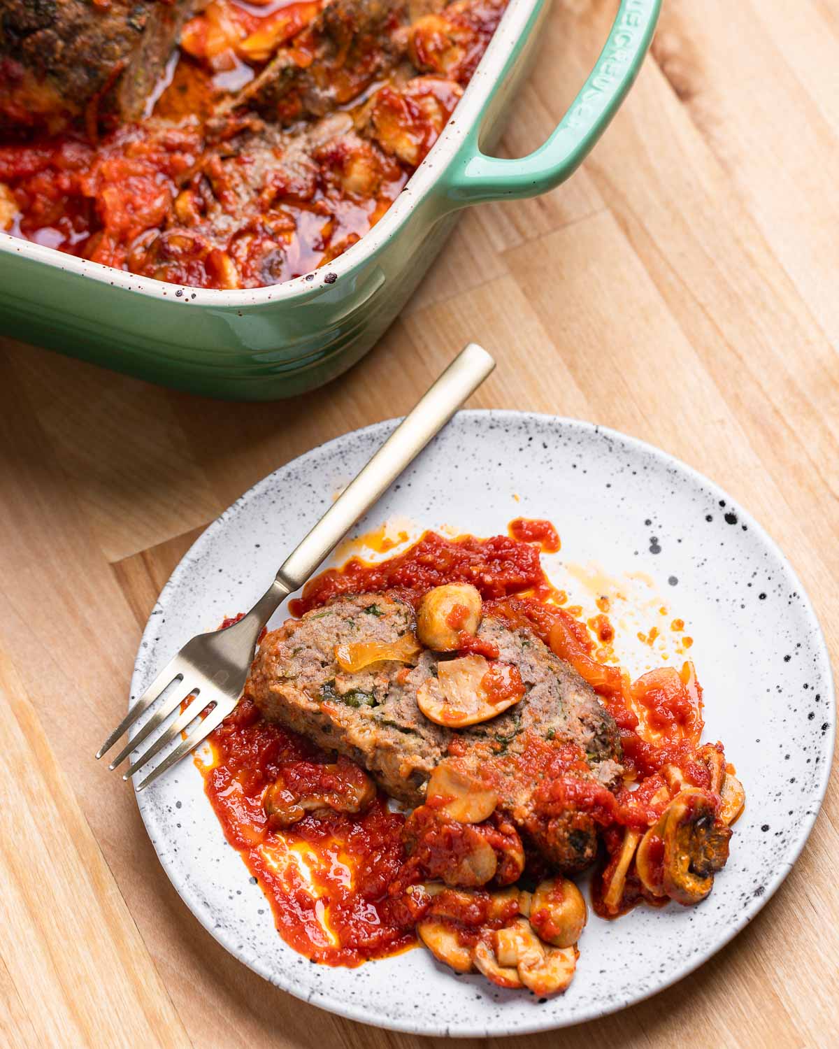 Slice of meatloaf in white plate with mushrooms and sauce on top.