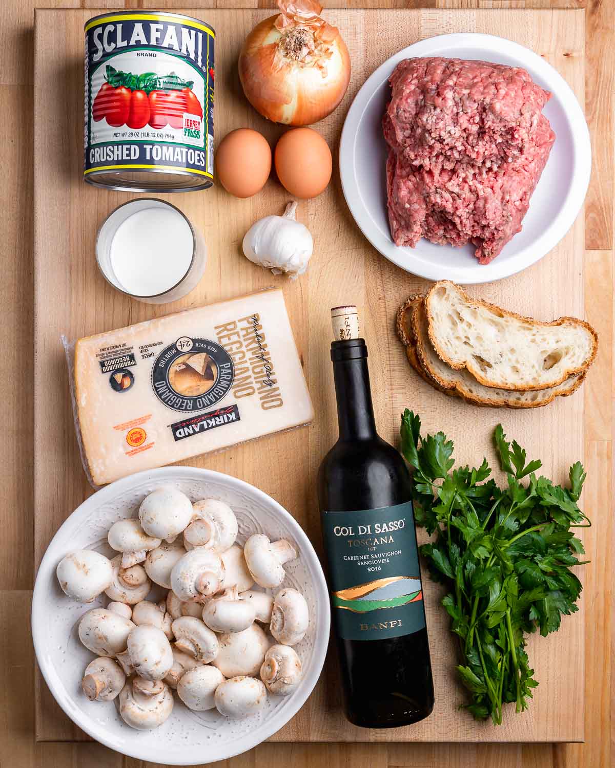 Ingredients shown: plum tomatoes, onion, garlic, eggs, beef, bread, cheese, mushrooms, red wine, and parsley.