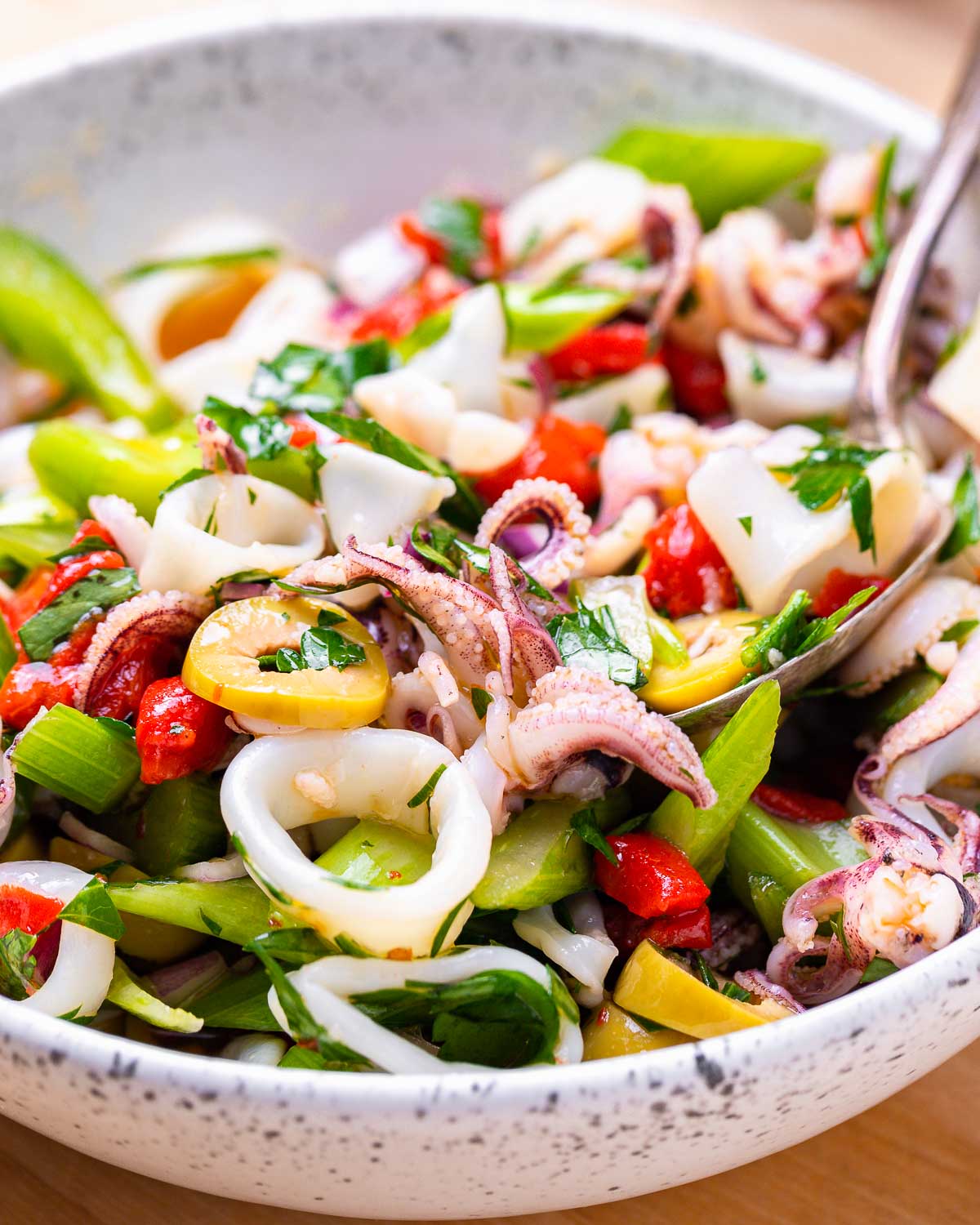 White bowl with Italian calamari salad and serving spoon.