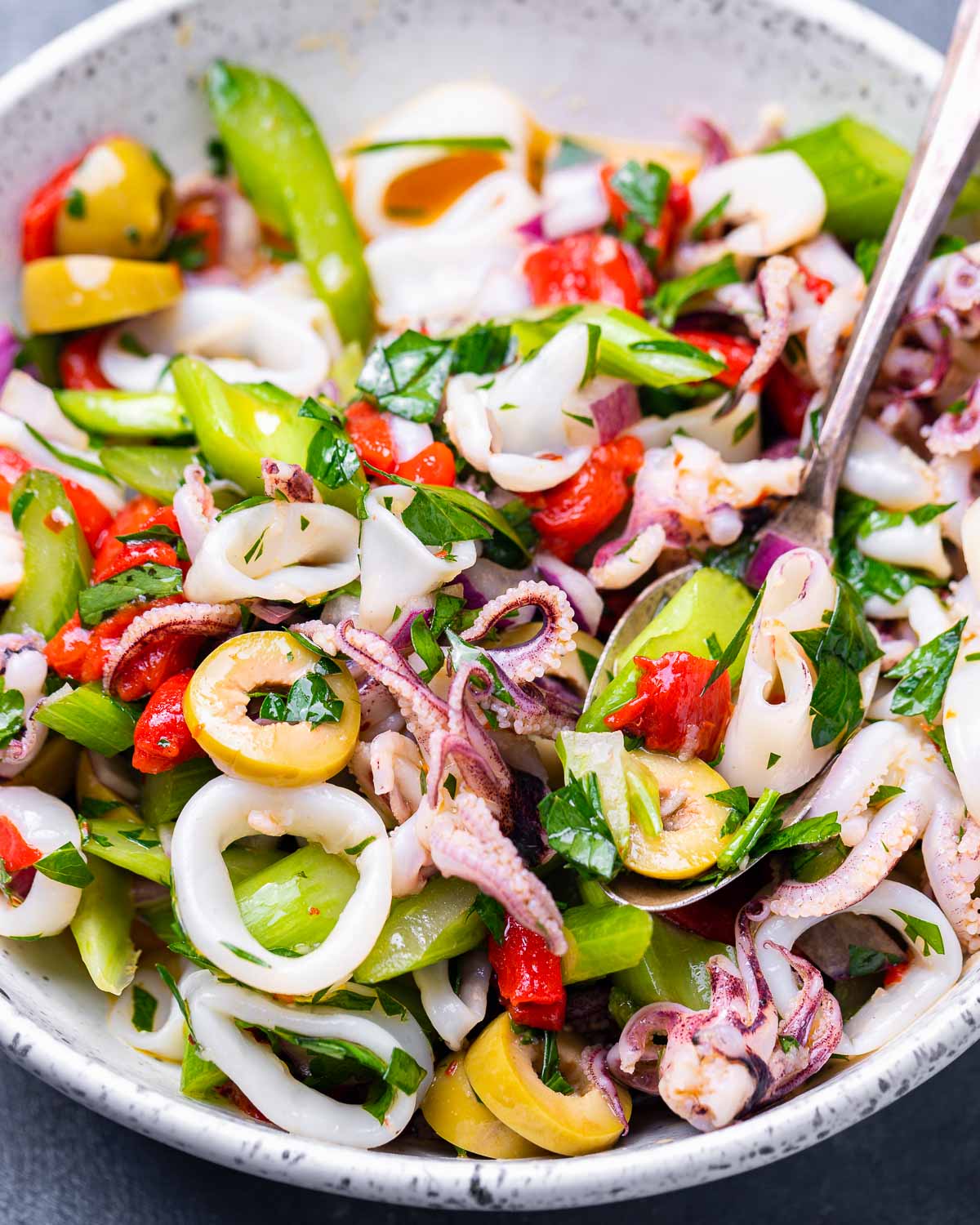 White bowl with Italian calamari salad and serving spoon on blue background.