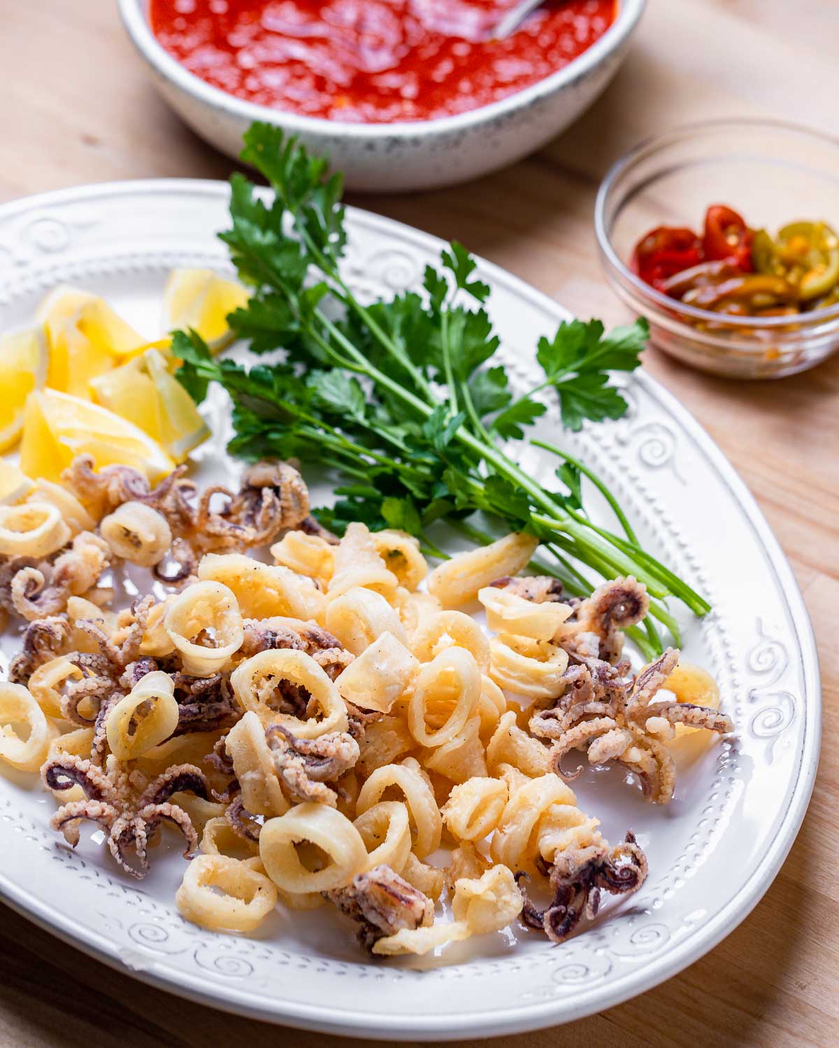 Plate with fried calamari and bowl of cherry peppers and marinara sauce.