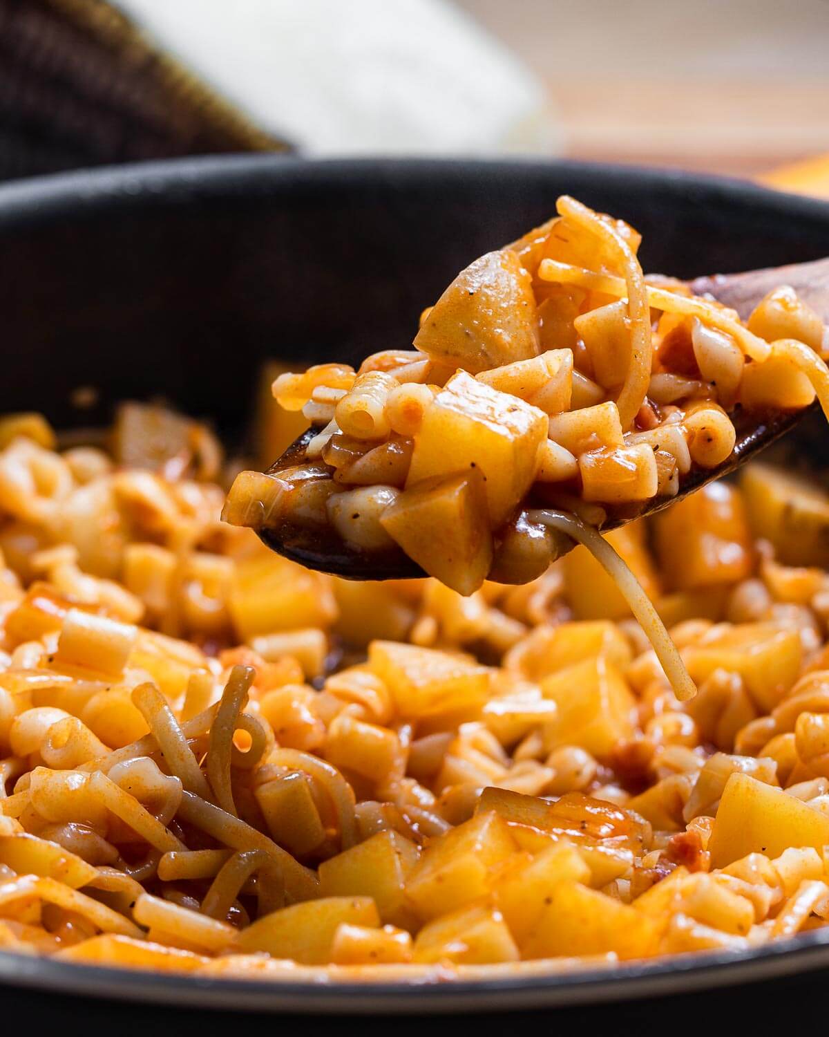 Wooden spoon holding pasta and potatoes.