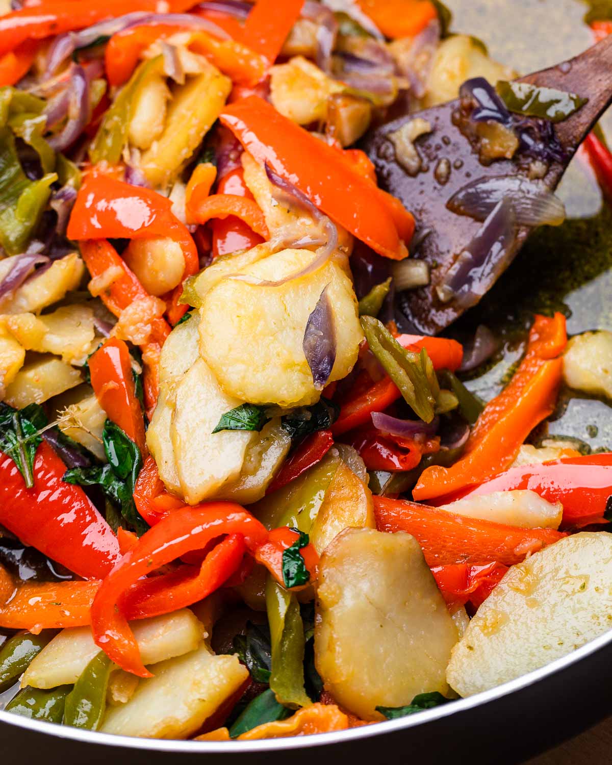 Wooden spoon scooping out potatoes and peppers.