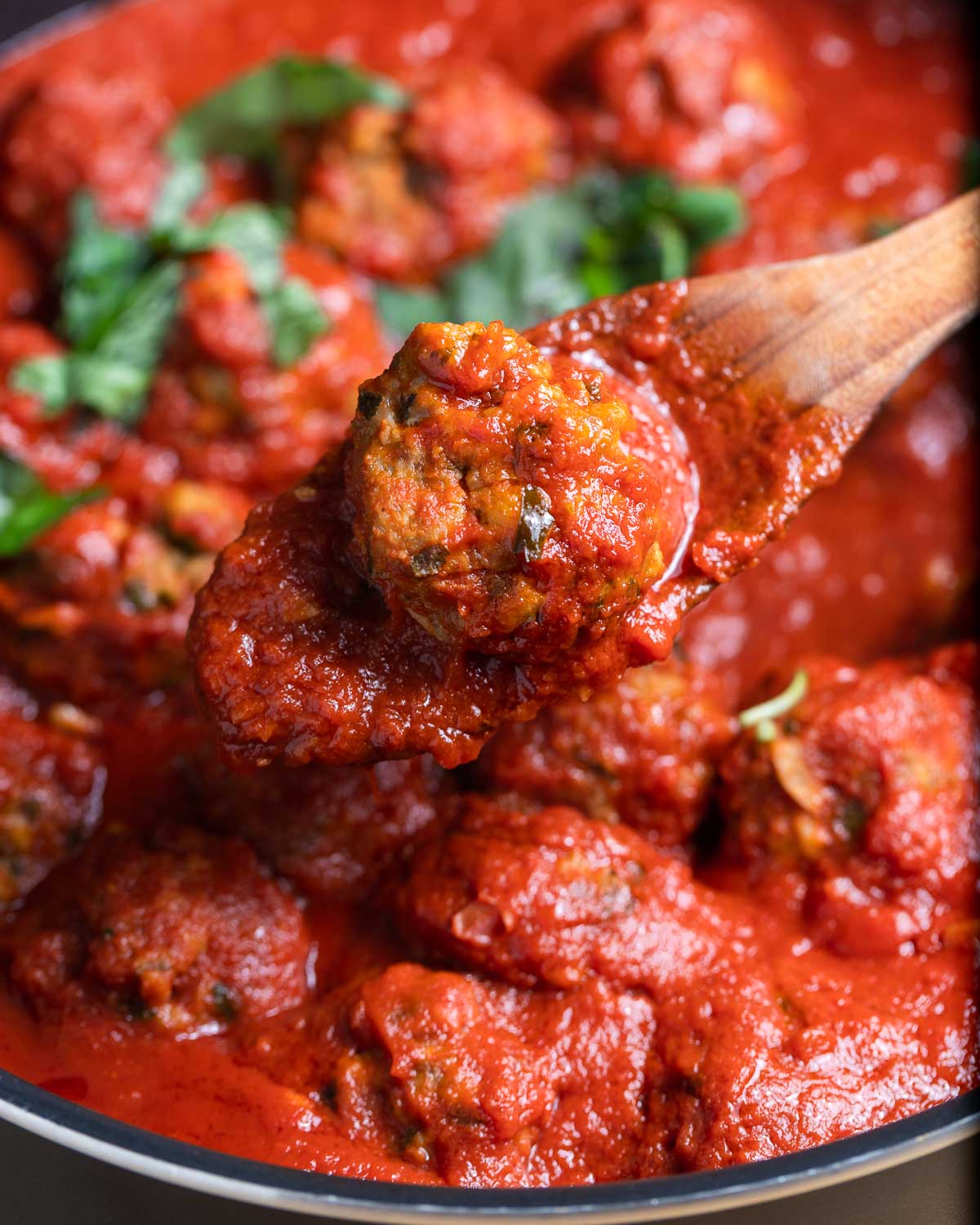 Sausage meatball held with wooden spoon.