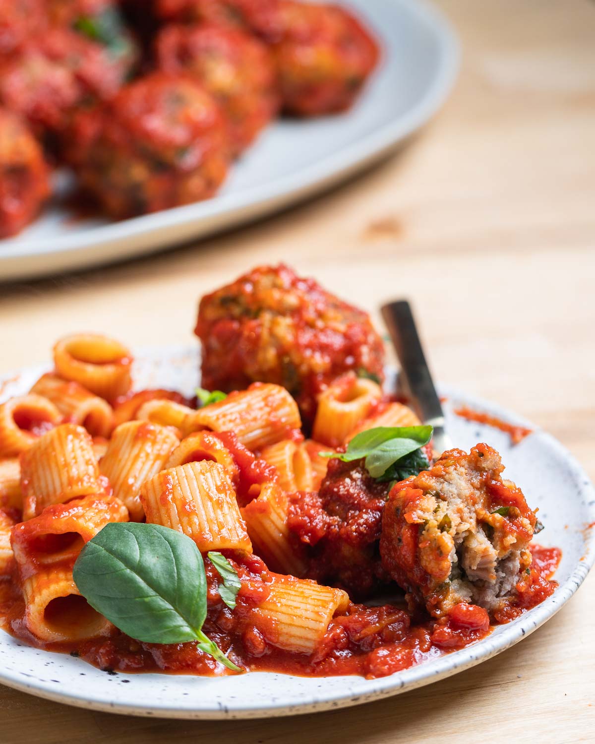 Cut in half sausage meatball with rigatoni and sauce on white plate.