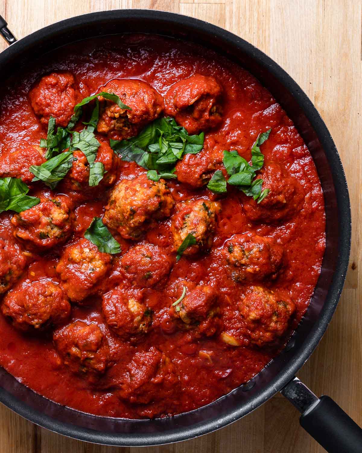 Sausage meatballs in large black pan with tomato sauce.