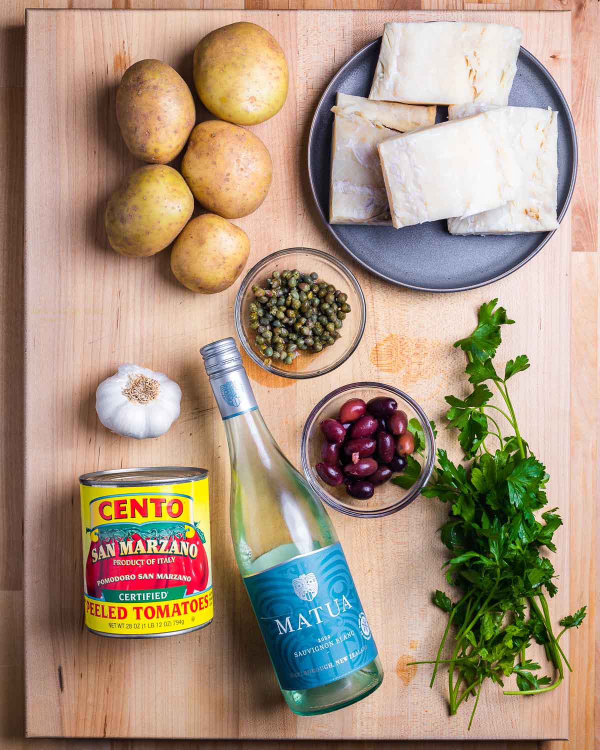 Ingredients shown: potatoes, baccala, capers, garlic, tomatoes, white wine, olives, and parsley.