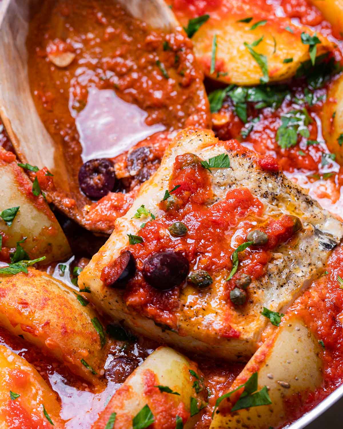 Piece of baccala in tomato sauce with large wooden spoon.