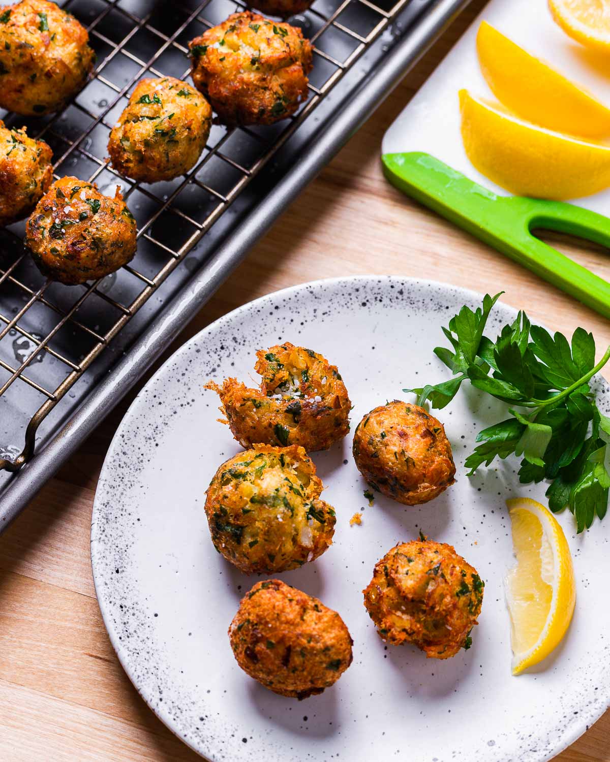 Baccala fritters on white plate and wire rack with lemon wedges on cutting board.