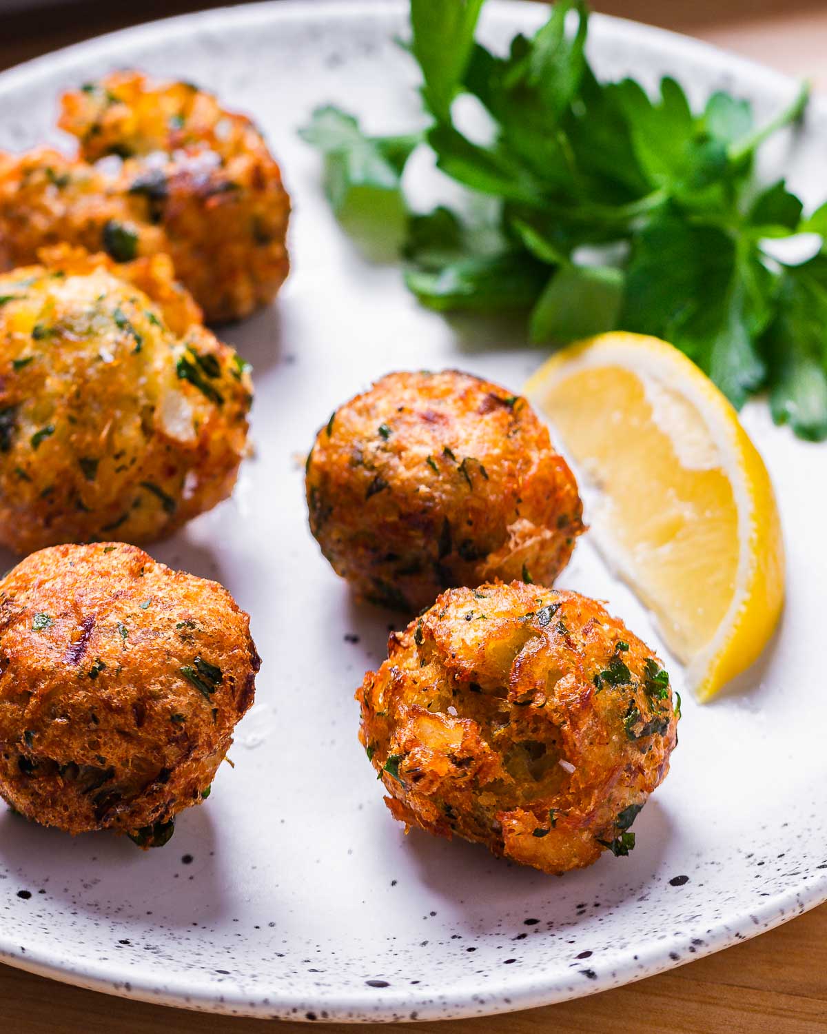 Baccala fritters in white plate with lemon wedge and parsley garnish.