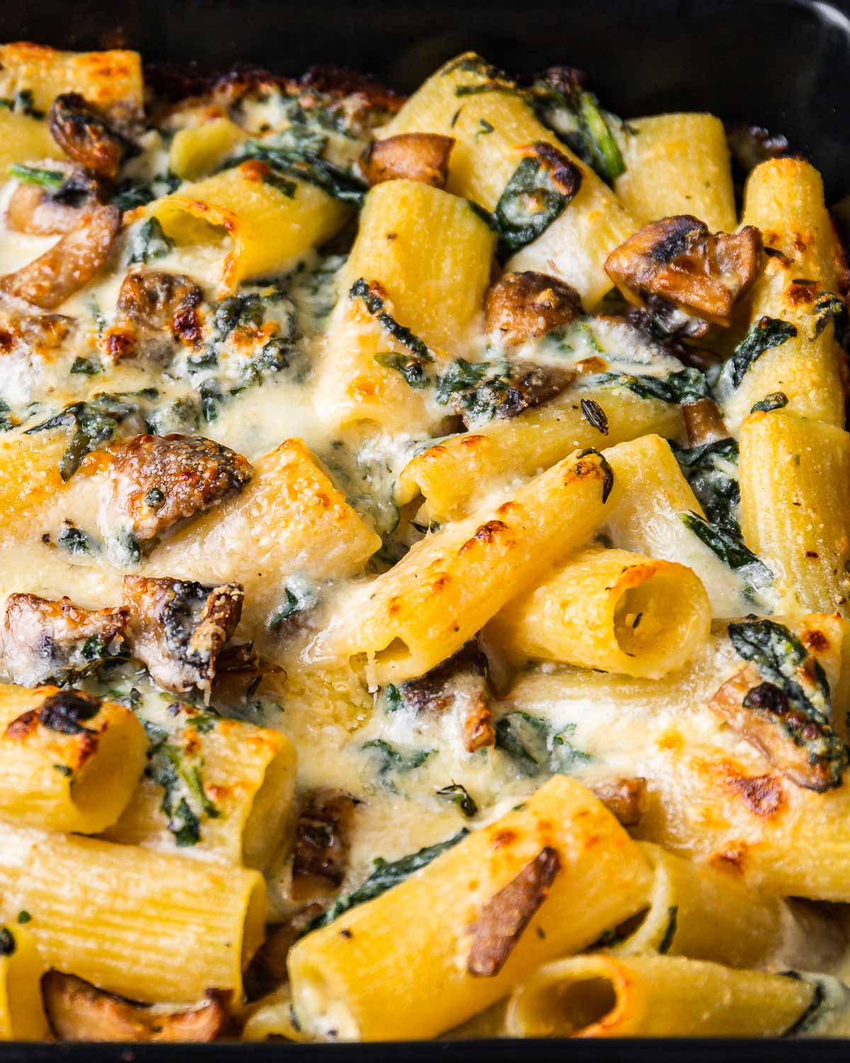 Baked rigatoni with spinach and mushrooms in baking dish.