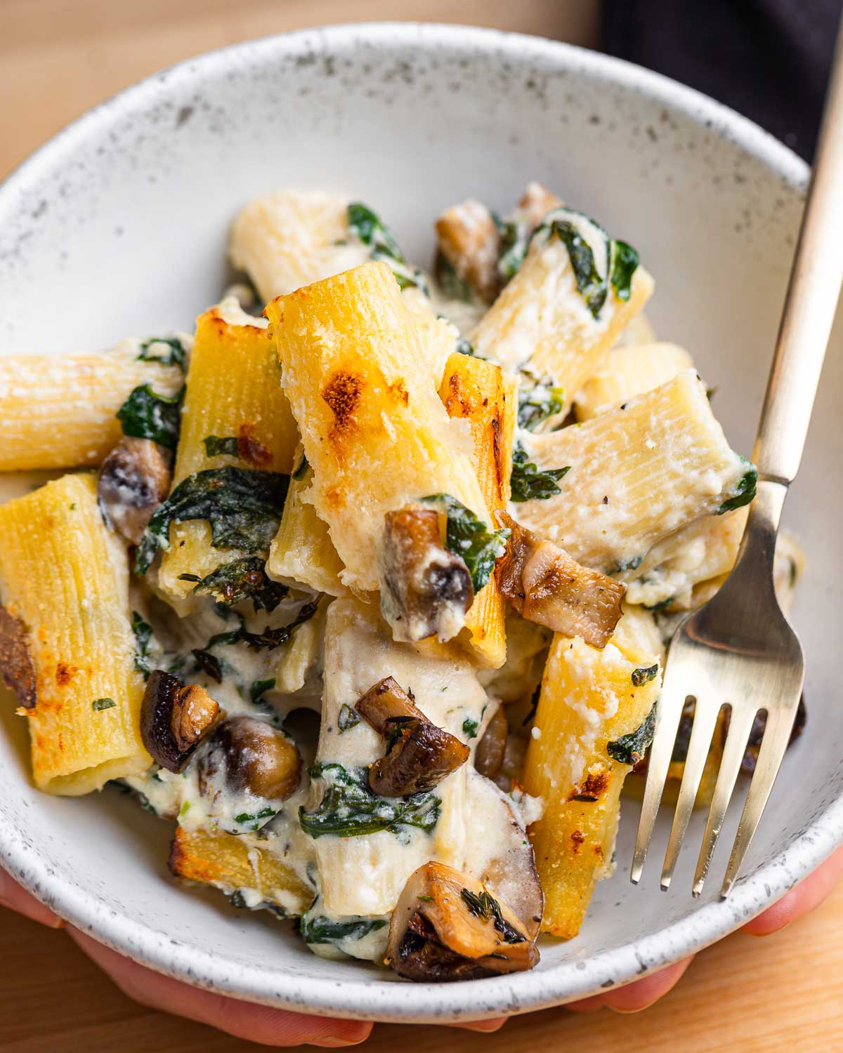 White bowl with baked pasta with mushrooms and spinach.