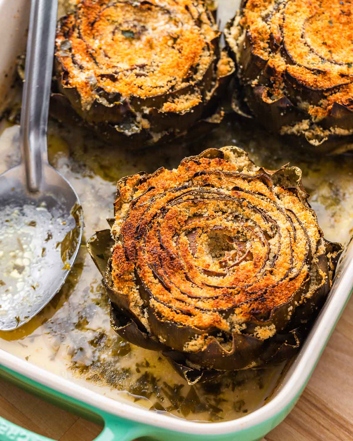 Cooked stuffed artichokes in baking dish.