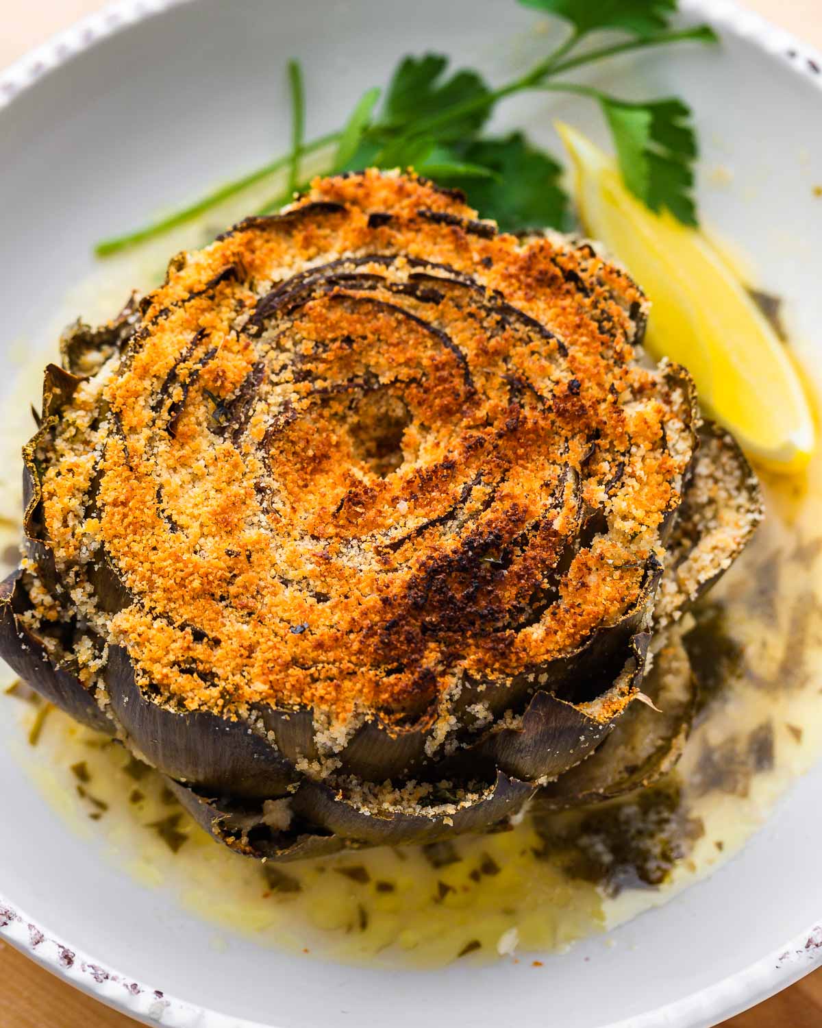 Stuffed artichoke on plate with lemon wedge and parsley.