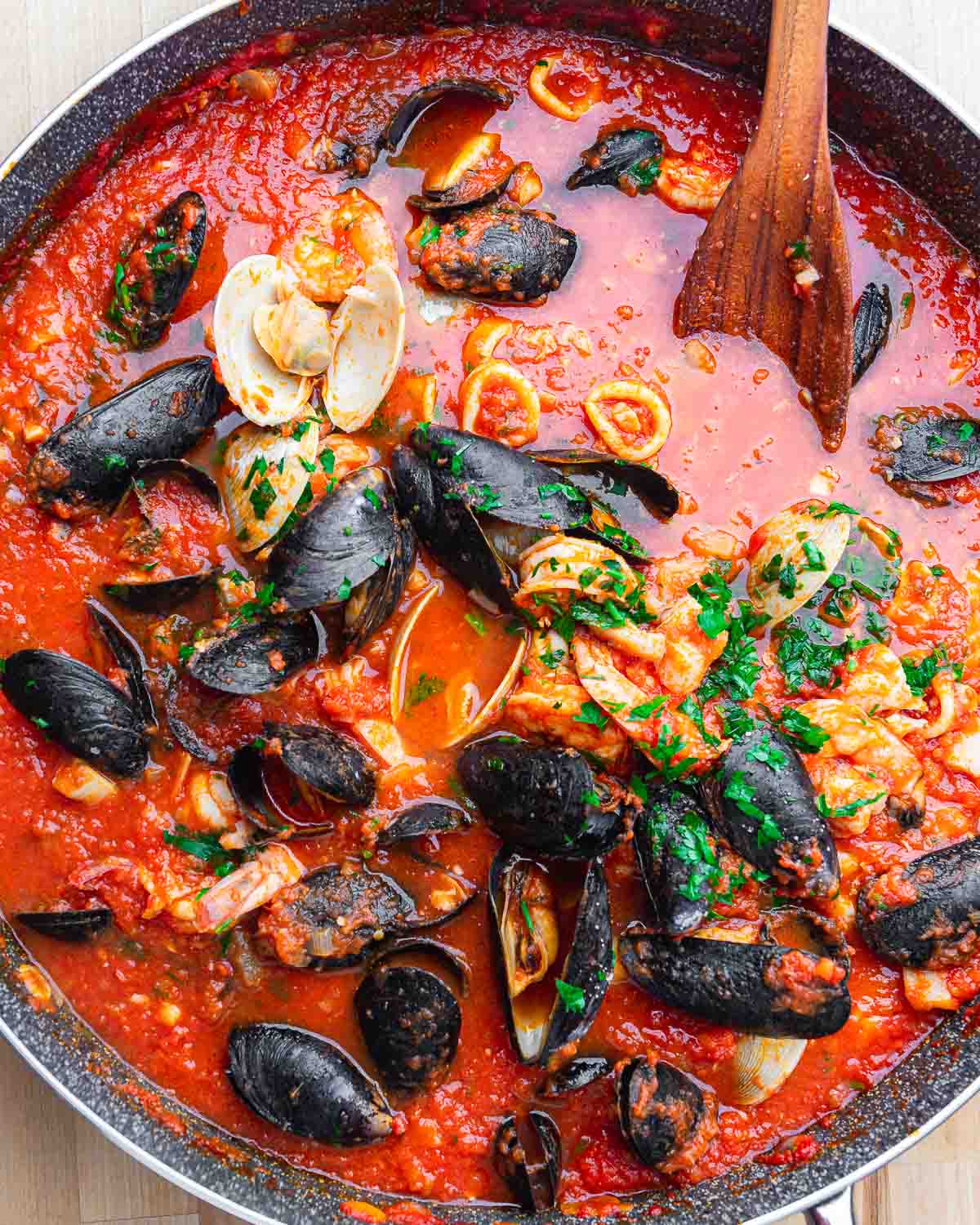 Overhead shot of large pan with clams, mussels, calamari, and fish in tomato sauce.