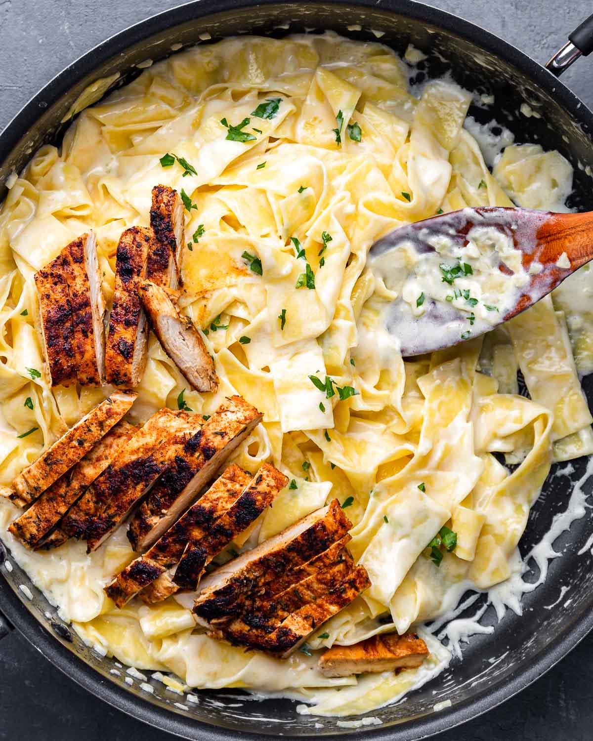 Overhead shot of alfredo pasta with pieces of blackened chicken on top.