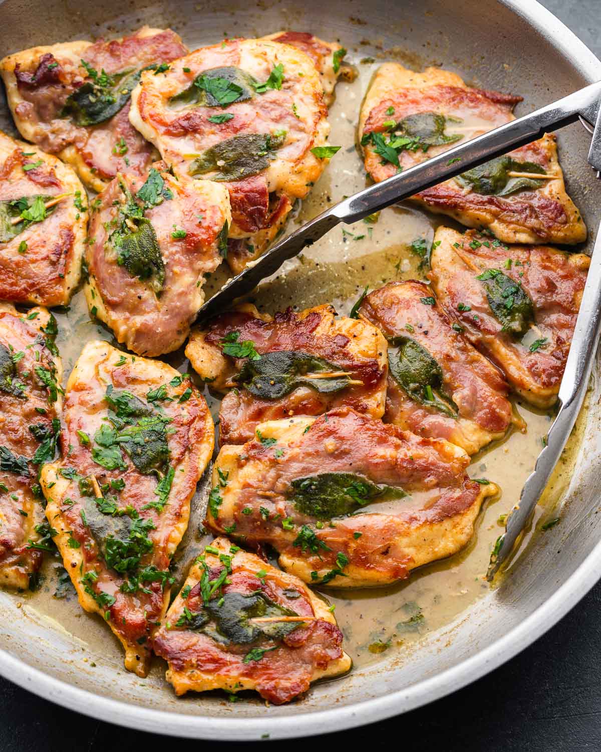 Large pan and tongs with finished chicken saltimbocca.