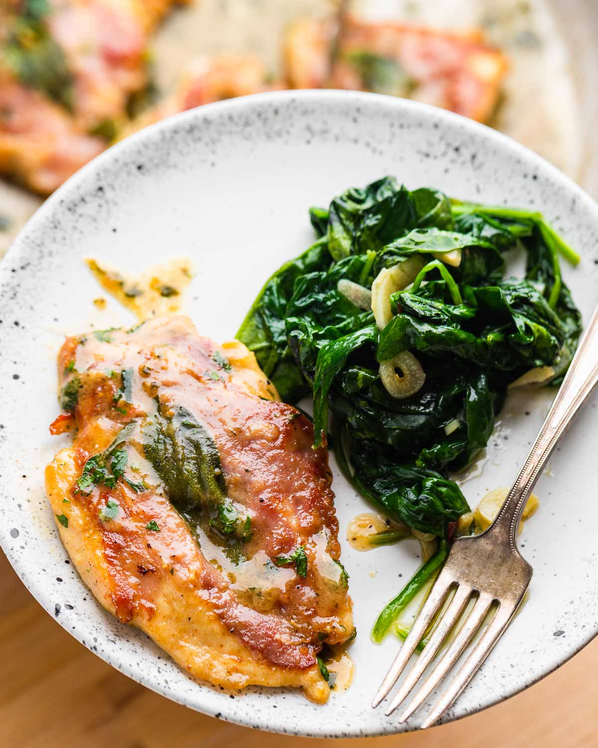 White plate held in hands with chicken saltimbocca and garlic spinach.