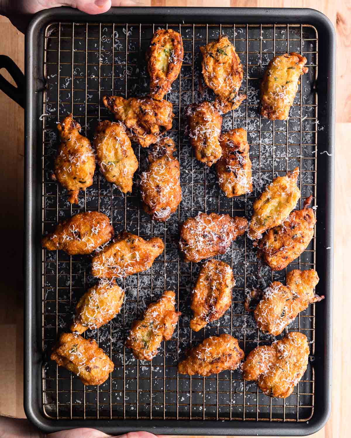 Hands holding baking sheet with fried artichoke hearts.