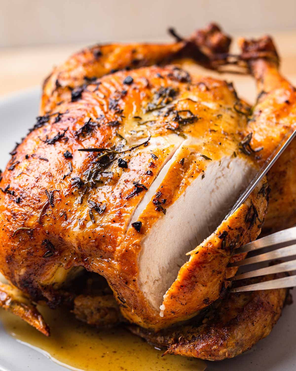 Roast chicken being sliced with fork and knife.