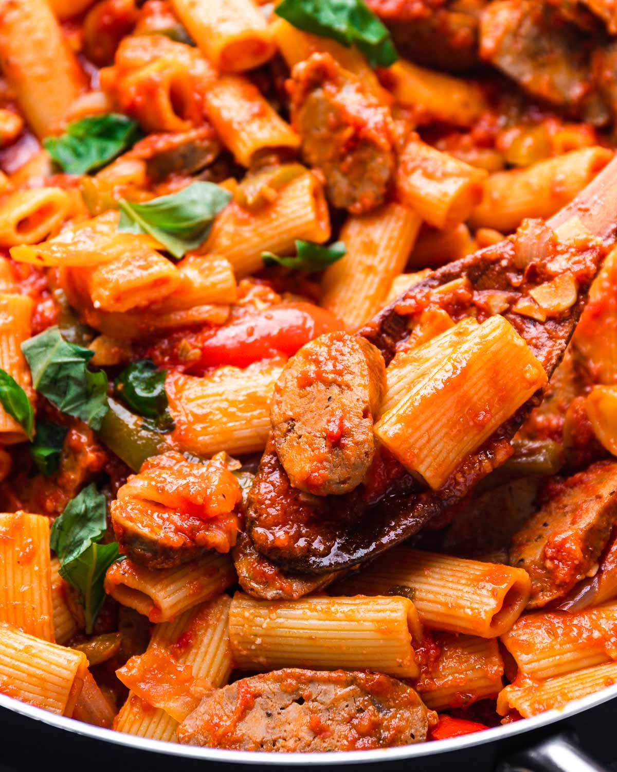 Wooden spoon holding rigatoni and sausage over pan.