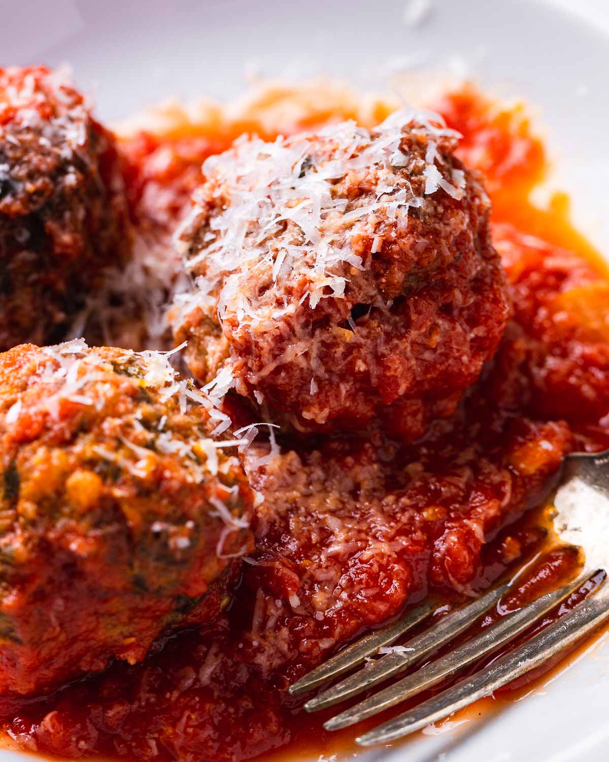 Sicilian meatballs in white plate with shaved Pecorino Romano.