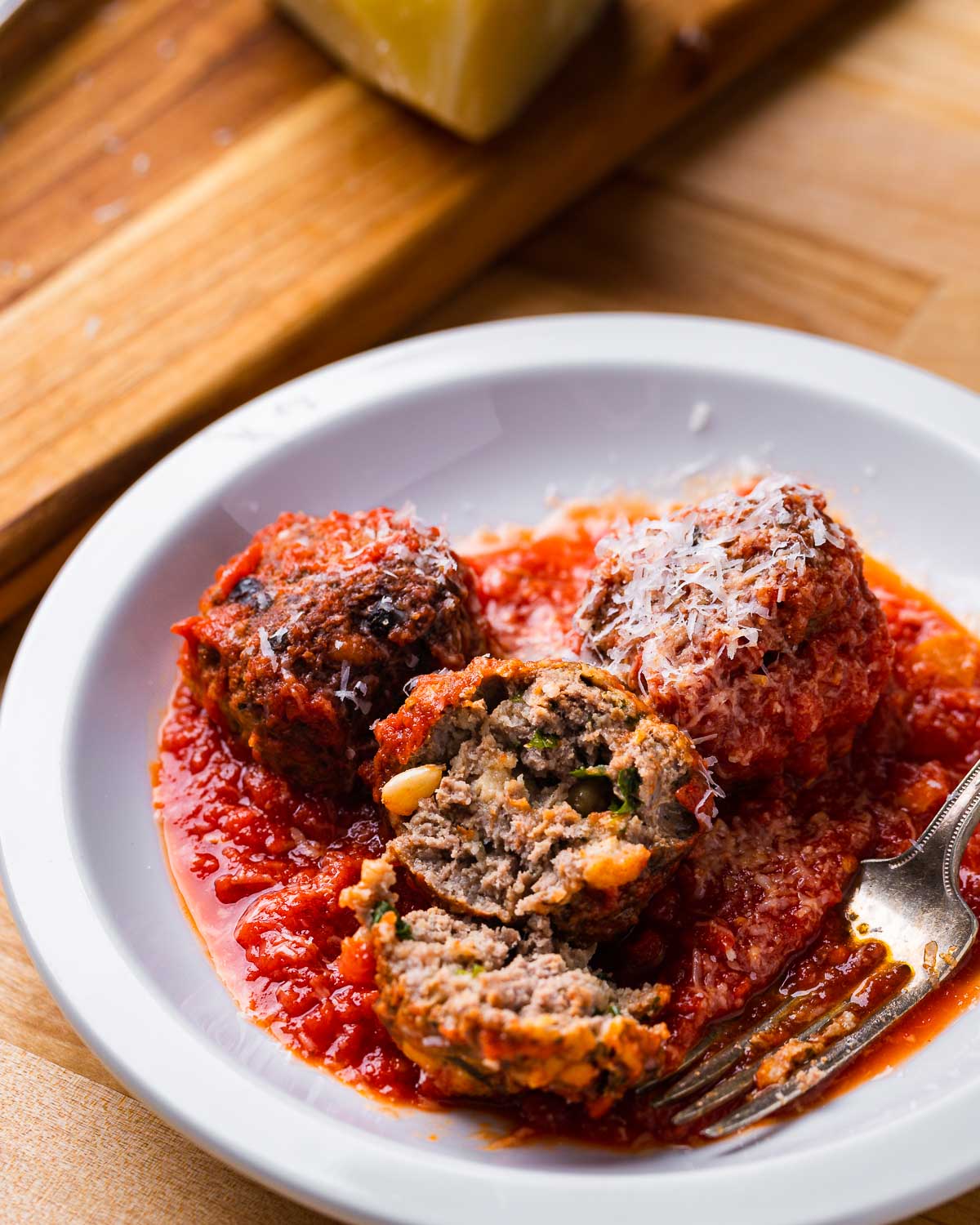 Sicilian style meatball with sauce cut in half in white plate.