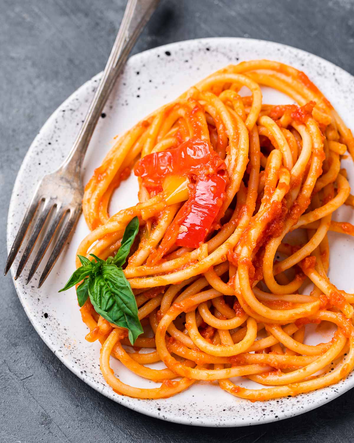 Bucatini with peppers and basil in white plate.