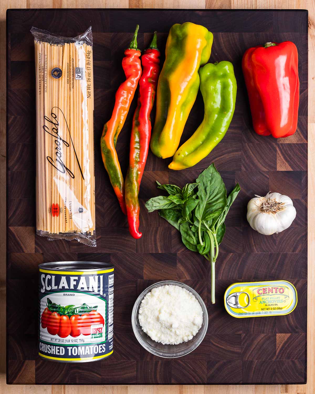 Ingredients shown: bucatini, peppers, basil, garlic, canned plum tomatoes, Pecorino Romano, and anchovies.