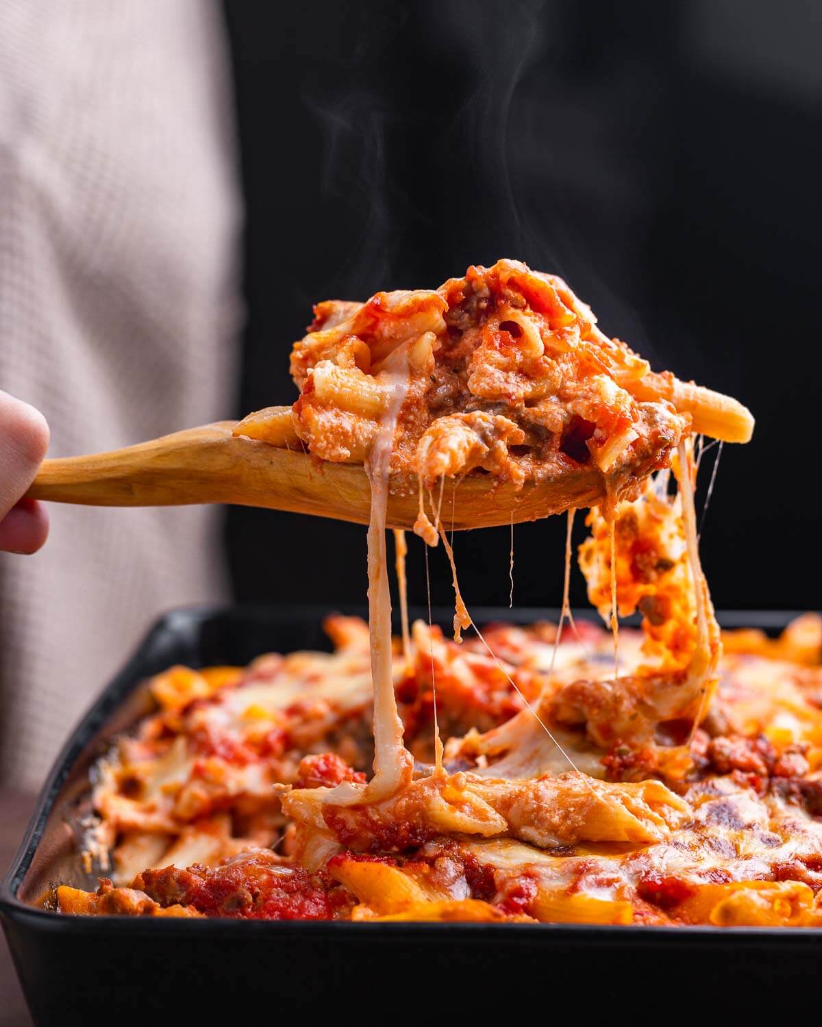Large wooden spoon holding baked pasta with cheese.