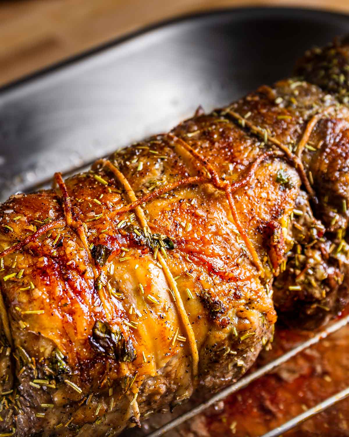 Cooked boneless leg of lamb on wire rack in roasting pan.