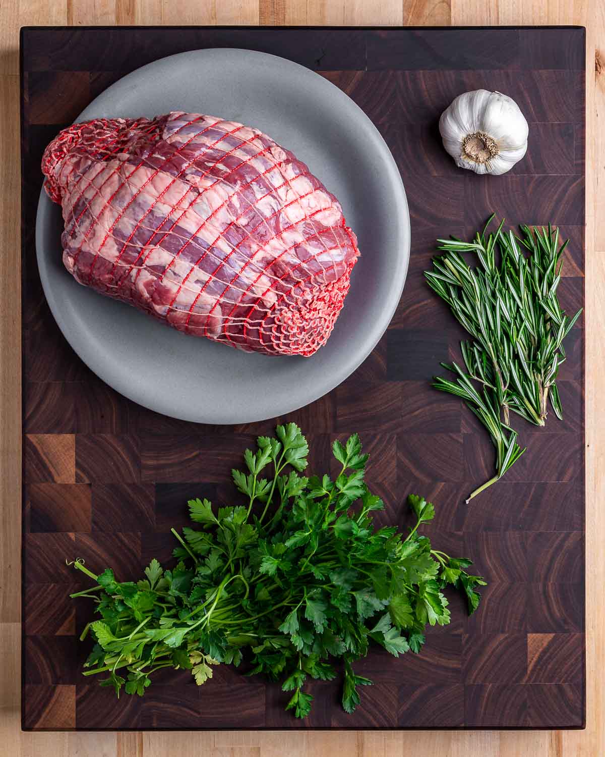 Ingredients shown: boneless leg of lamb, garlic, rosemary, and parsley.