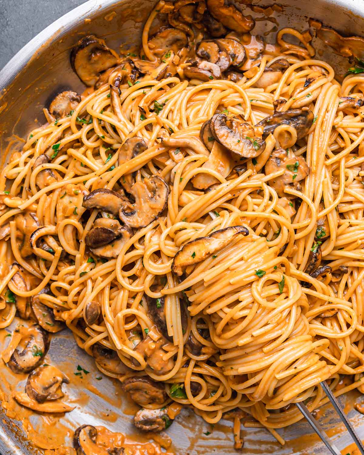 Mushroom brandy cream sauce spaghetti twirled in pan with pasta tweezers.
