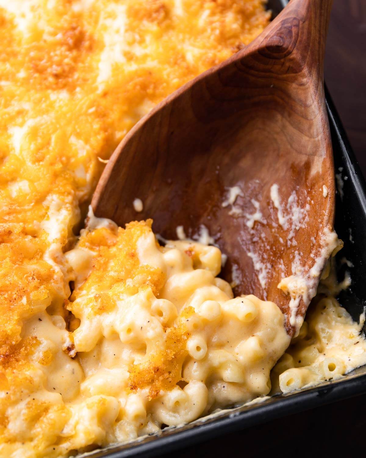 Large wooden spoon in in baking dish with baked mac and cheese.