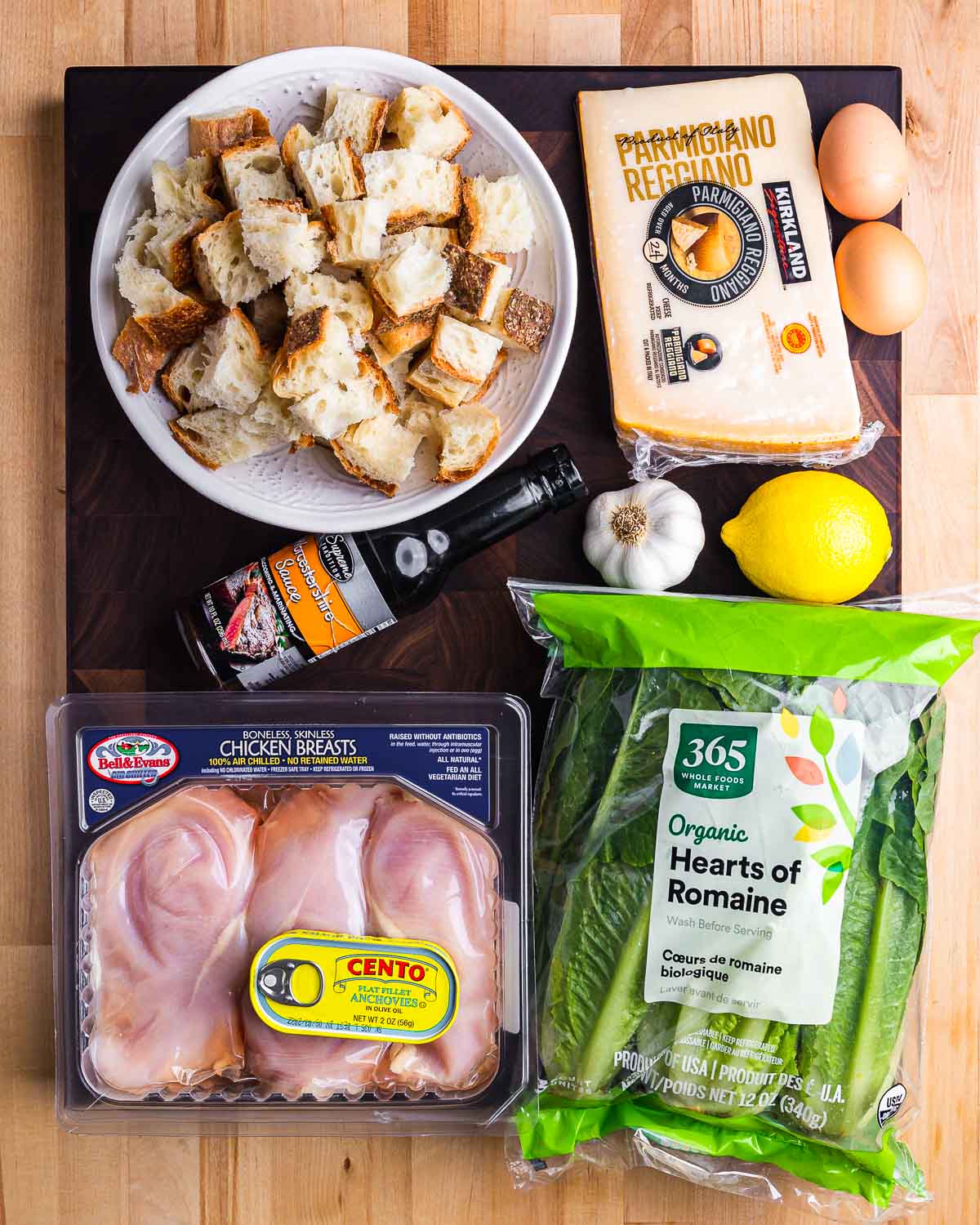 Ingredients shown: bread, parmesan, eggs, worcestershire, garlic, lemons, chicken breasts, anchovies, and romaine lettuce.