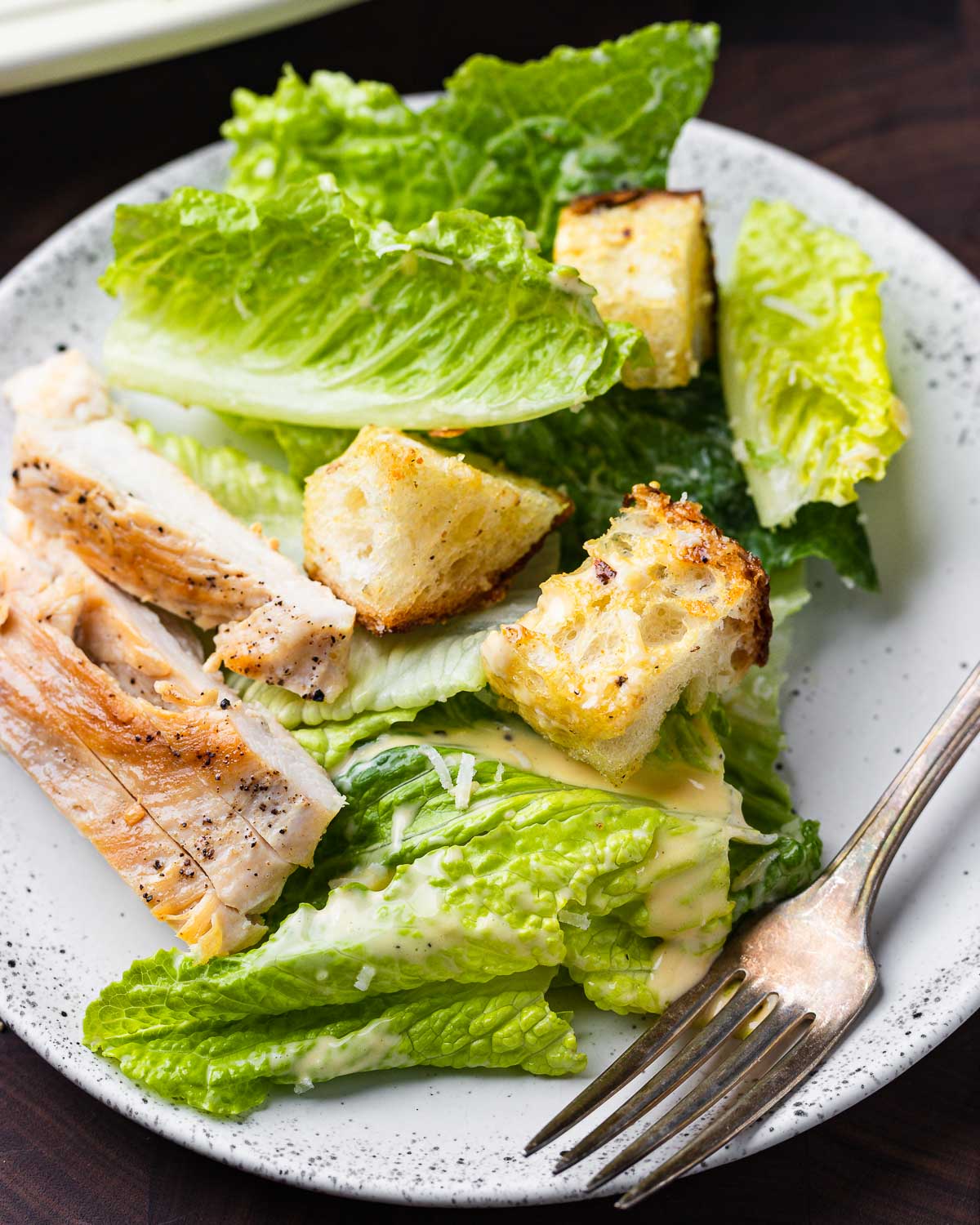 Chicken Caeser salad in white plate on brown board.