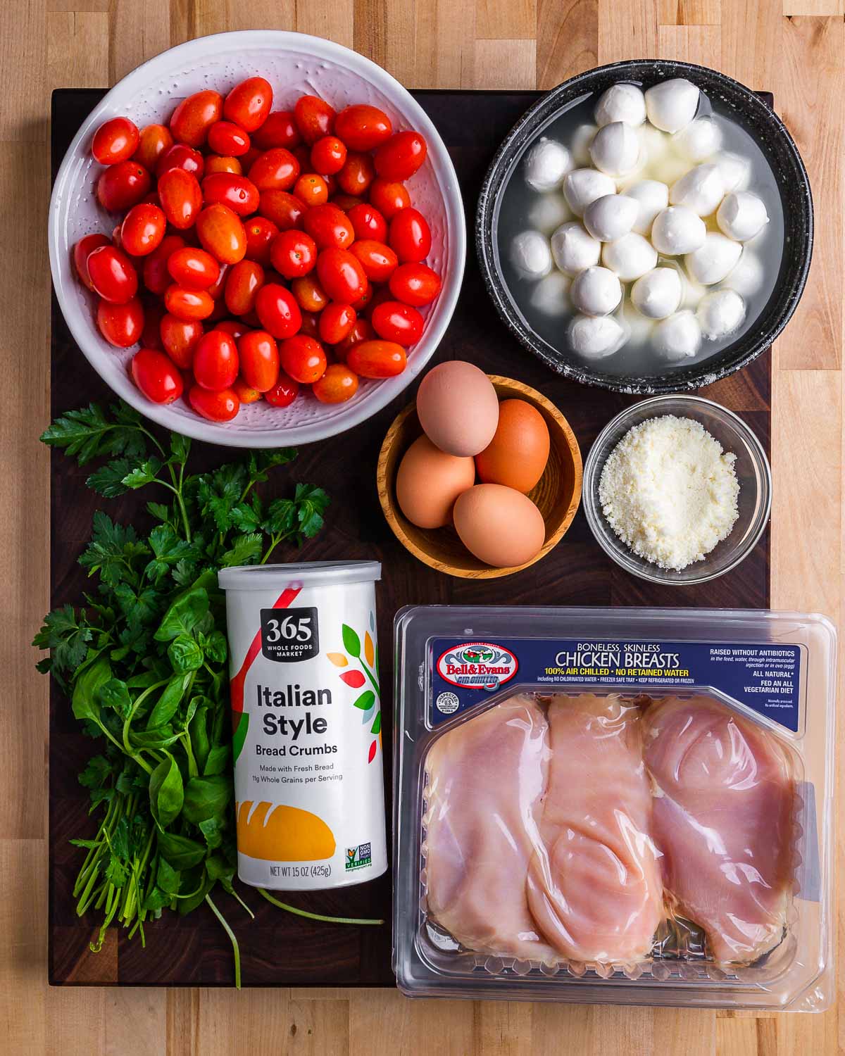 Ingredients shown: cherry tomatoes, mozzarella balls, parsley, breadcrumbs, eggs, Pecorino, and chicken cutlets.