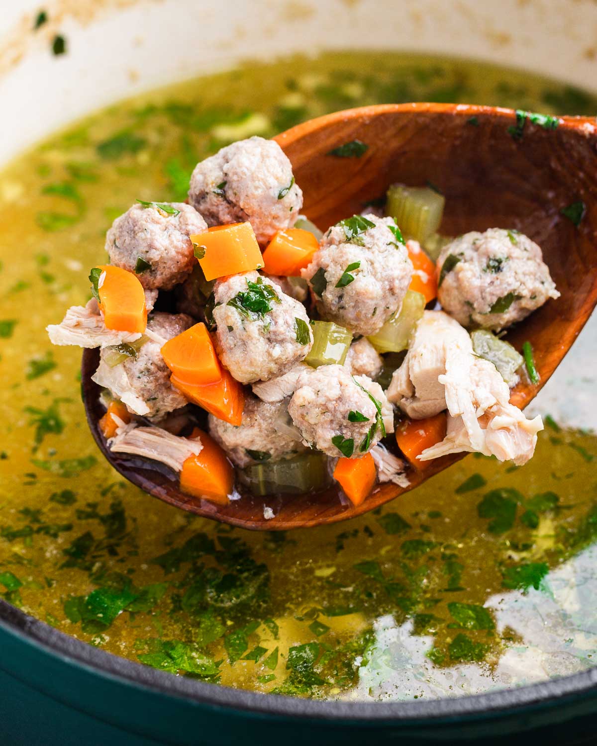 Large wooden ladle holding tiny meatballs over soup pot.