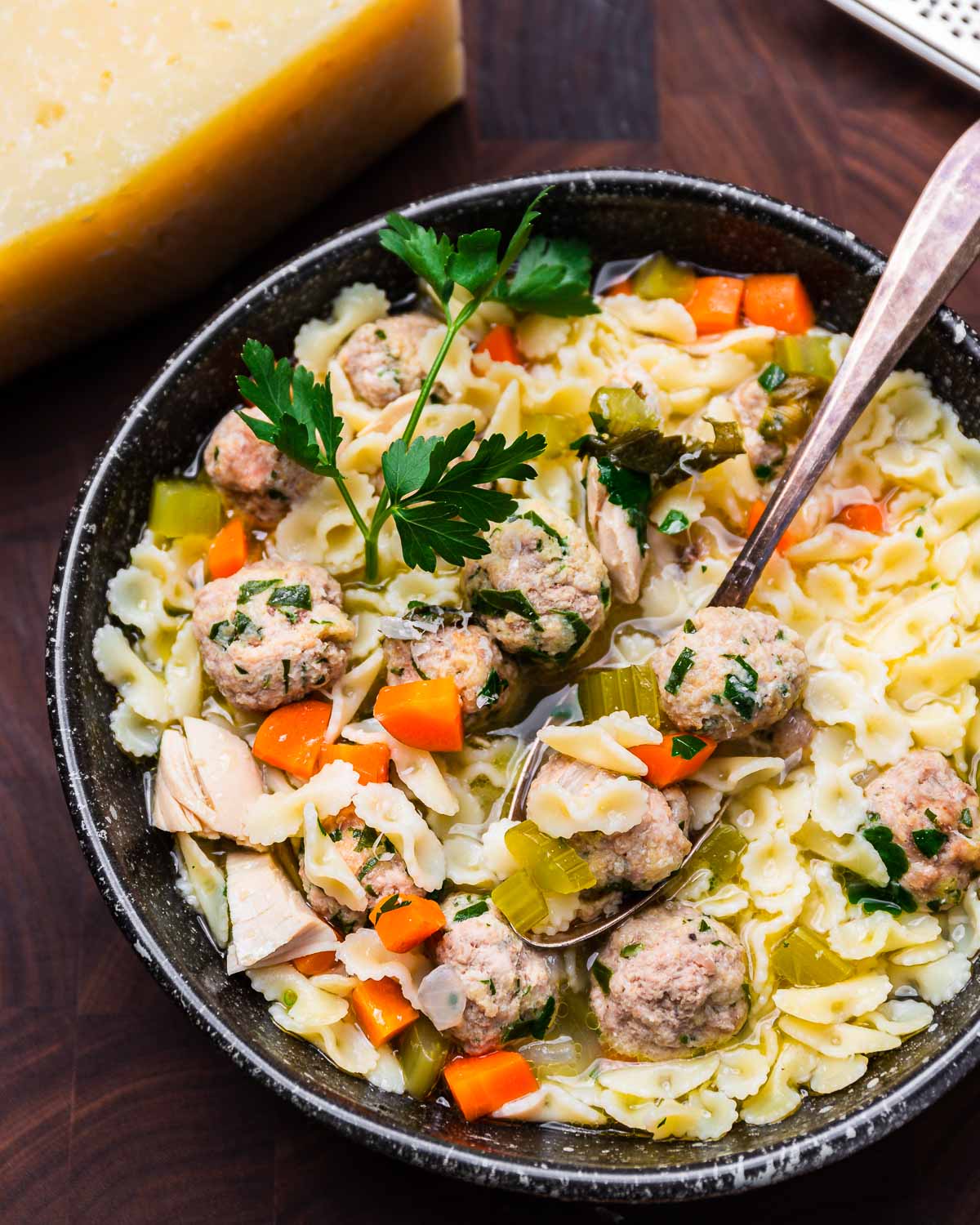 Chicken farfalline soup with meatballs in black bowl.