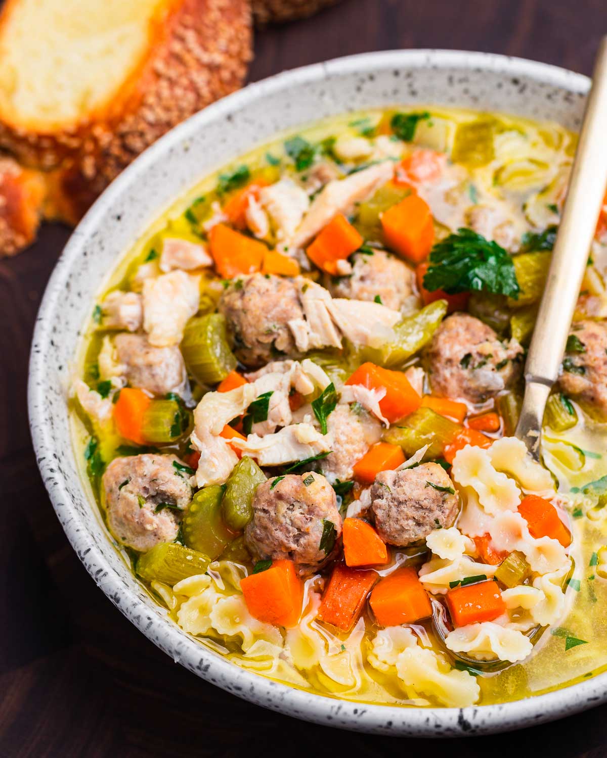 Chicken noodle soup with meatballs in white bowl on wooden board.