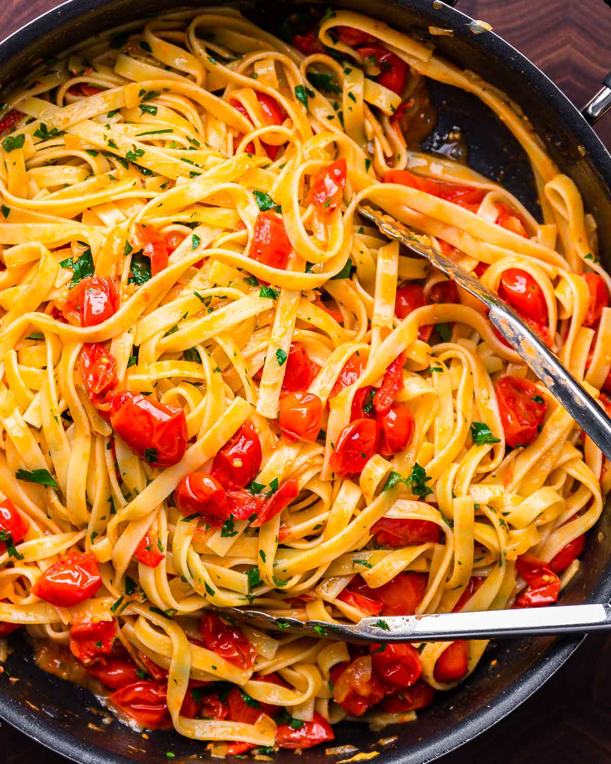 Fettuccine with cherry tomato butter sauce in black pan.