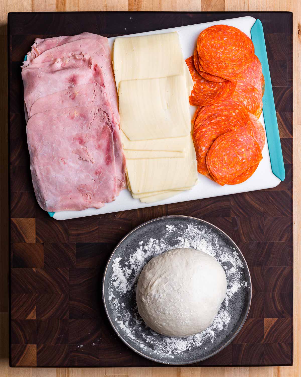 Ingredients shown: cutting board with ham, mozzarella, and pepperoni and bowl with pizza dough ball.