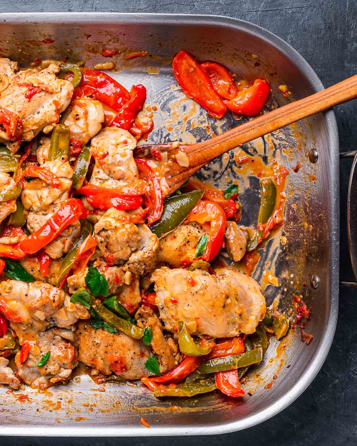 Chicken and peppers in large roasting pan on blue background.