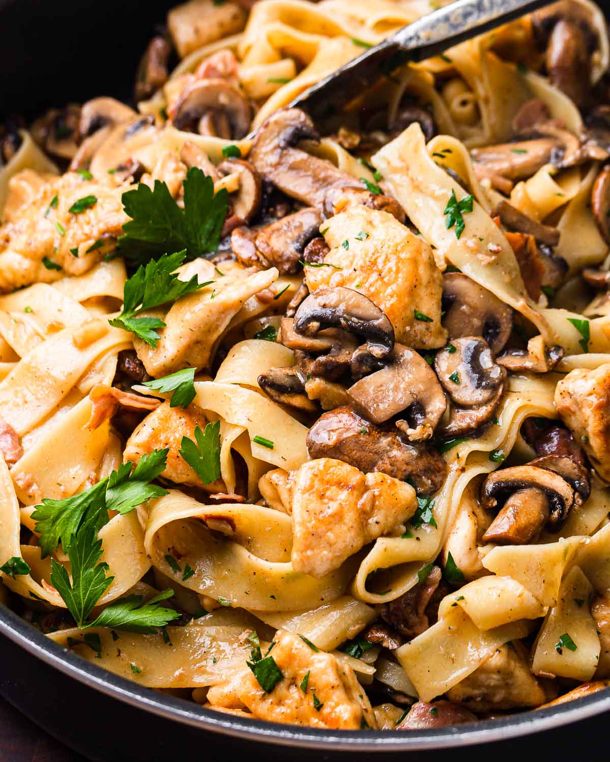 Chicken marsala pasta in black pan with tongs.