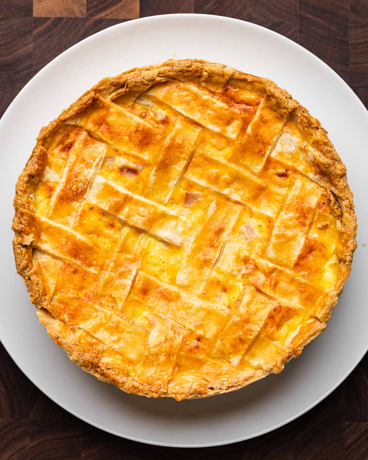 Cooked Easter pie (pizzagaina) in white plate on brown cutting board.