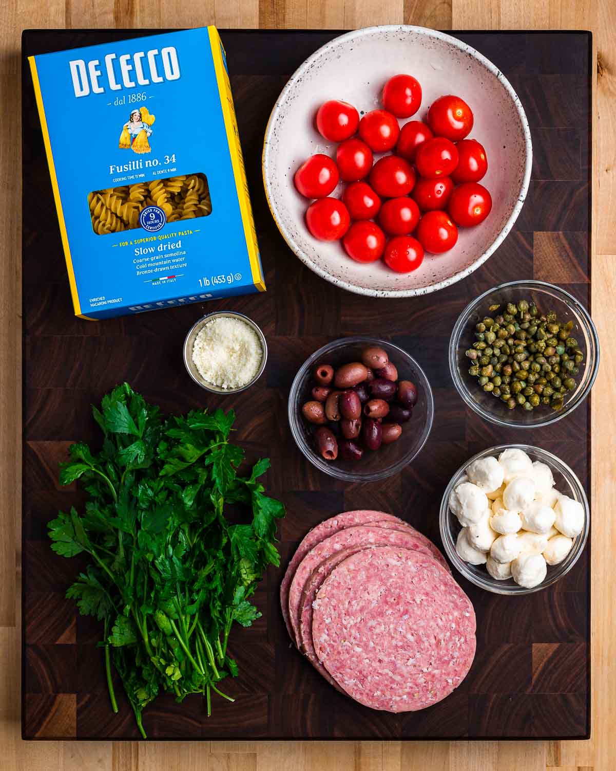 Ingredients shown: fusilli, tomatoes, Pecorino, parsley, olives, capers, salami, and mozzarella.