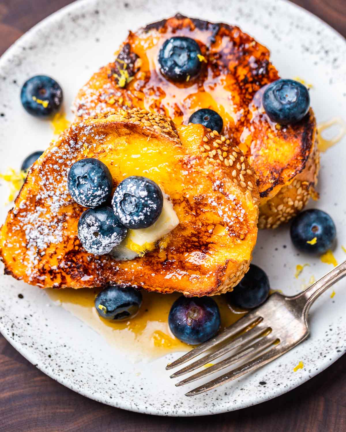 Lemon blueberry French toast with butter and syrup in white plate on wood board.