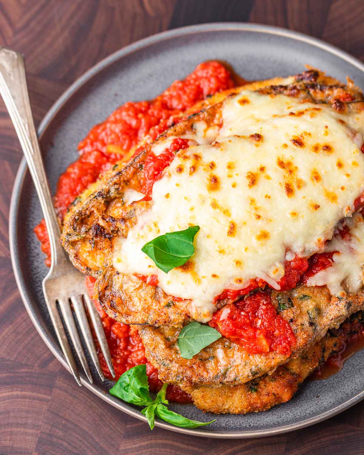 Chicken eggplant parmesan in grey plate on wood cutting board.